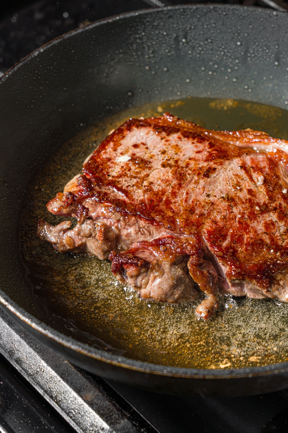 A skillet with steak cooking in oil.