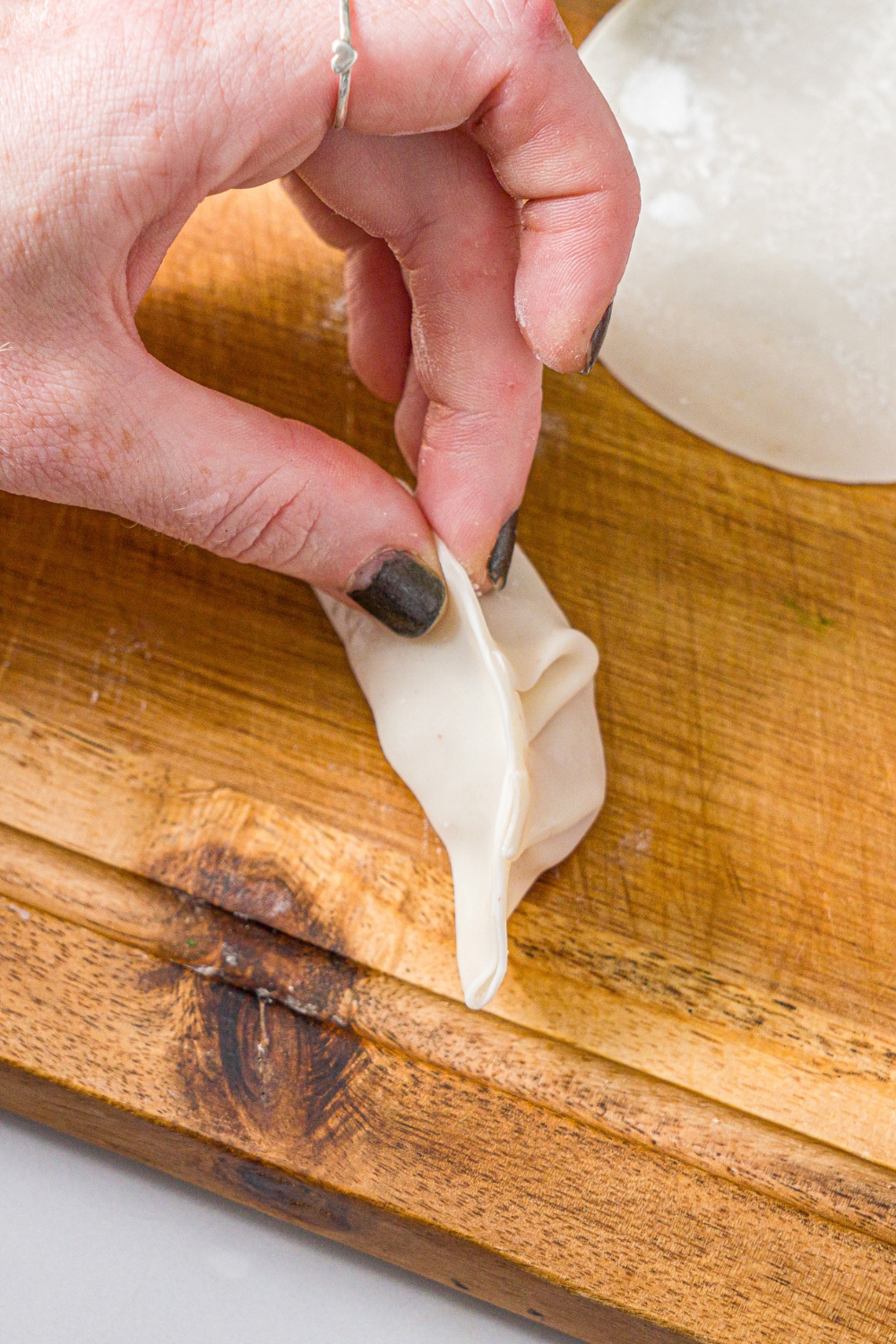 A hand folding a dumpling wrapper over a pork mixture to make pork dumplings.
