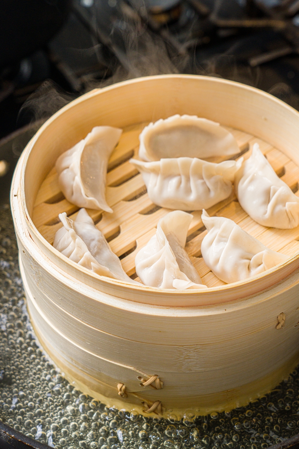 A steam basket with several pork dumplings steaming with hot water.