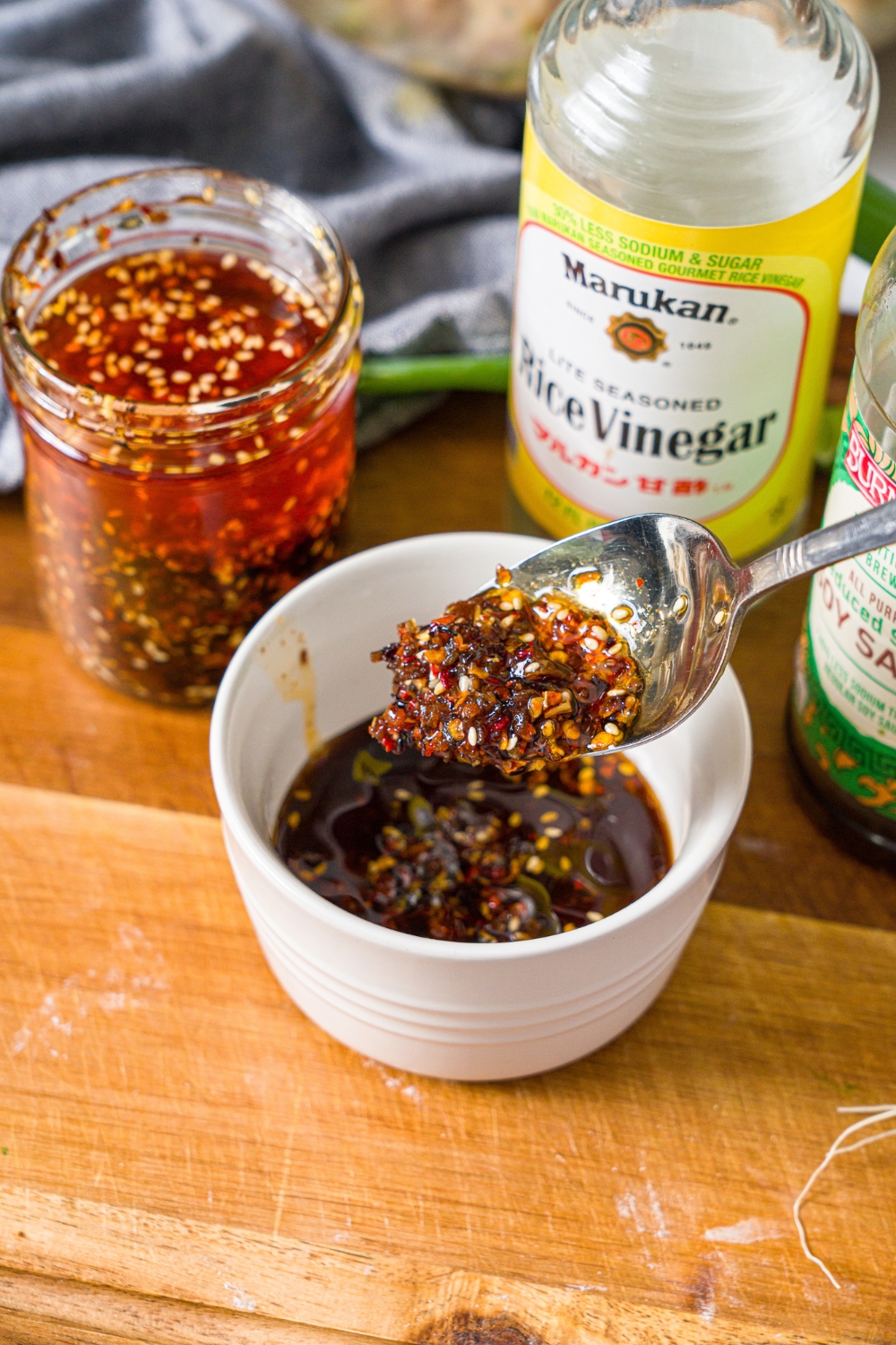 A small bowl with a spoon mixing chili oil sauce. The bowl is on a wooden board with additional ingredients.