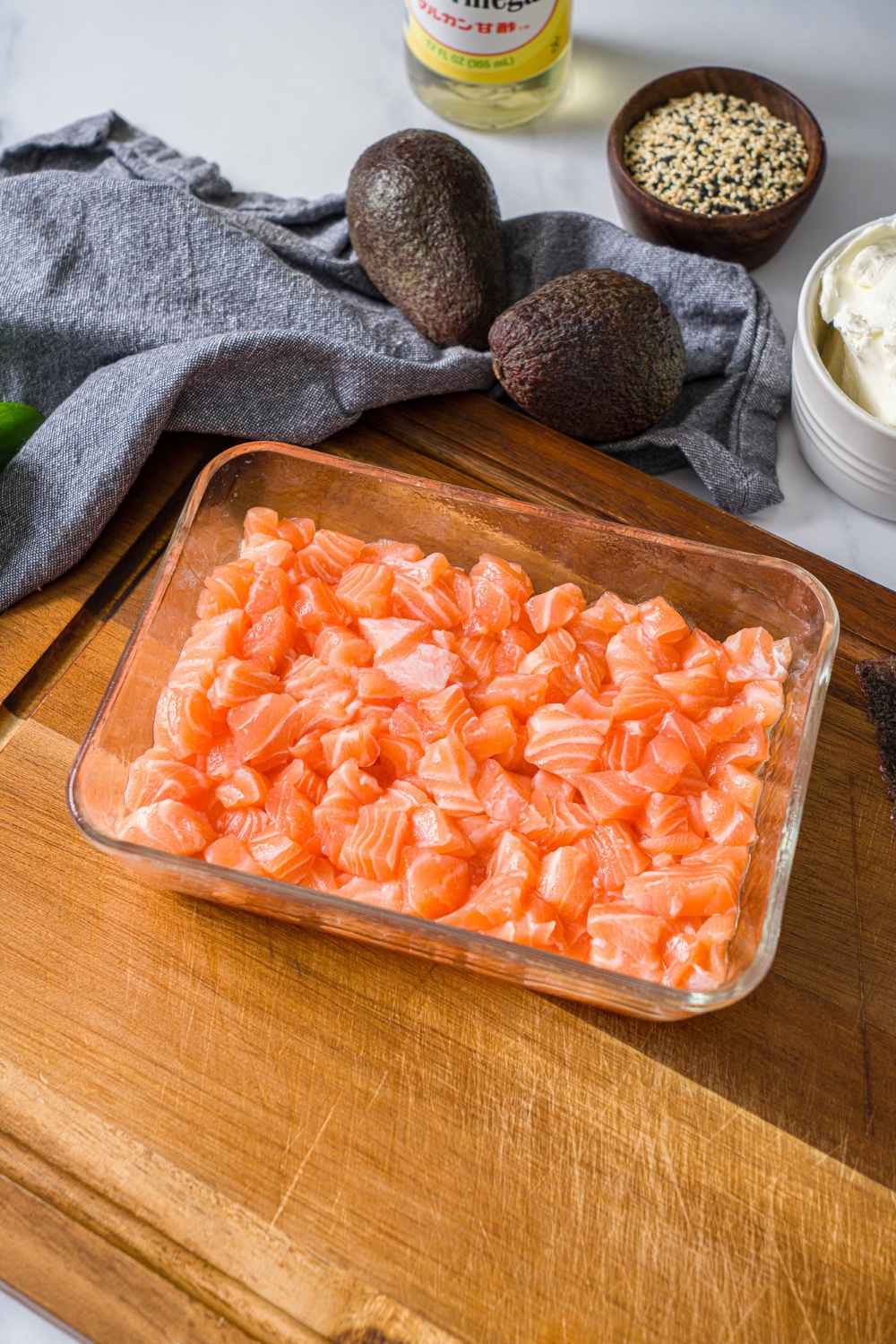 A glass baking dish covered with cubed sushi salmon. The dish is on a wooden board.