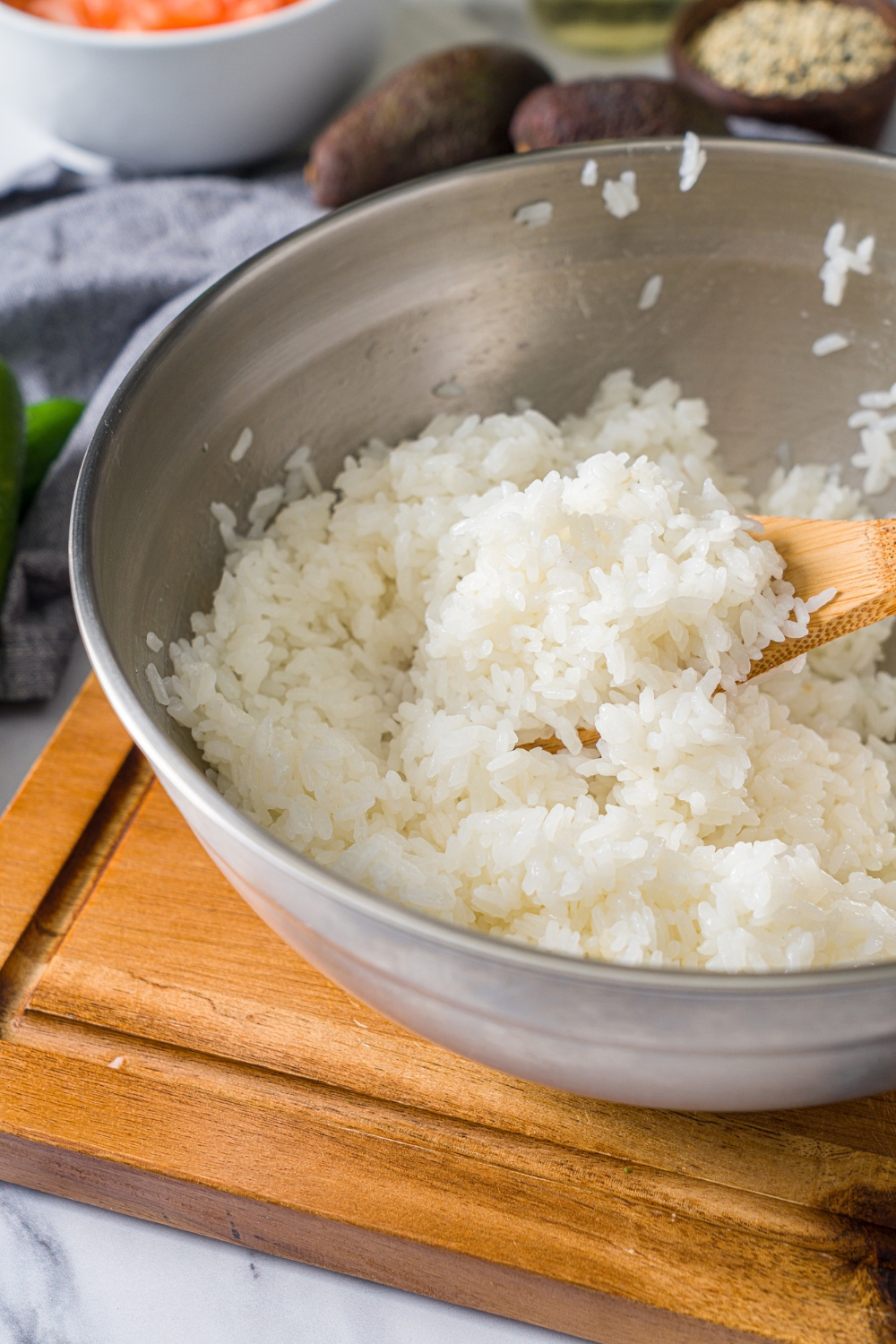 A large bowl with a wooden spoon mixing cooked rice and seasonings. The bowl is on a wooden board.