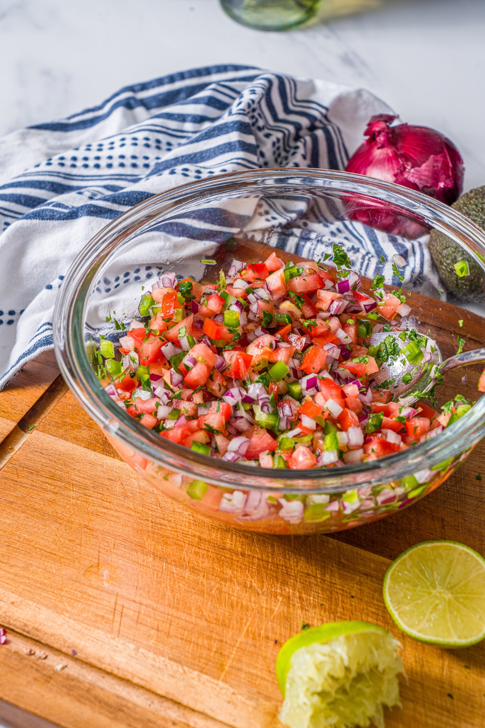A glass bowl with pico de gallo including diced tomatoes, red onion, and parsley. The bowl is on a wooden board with a squeezed lime.