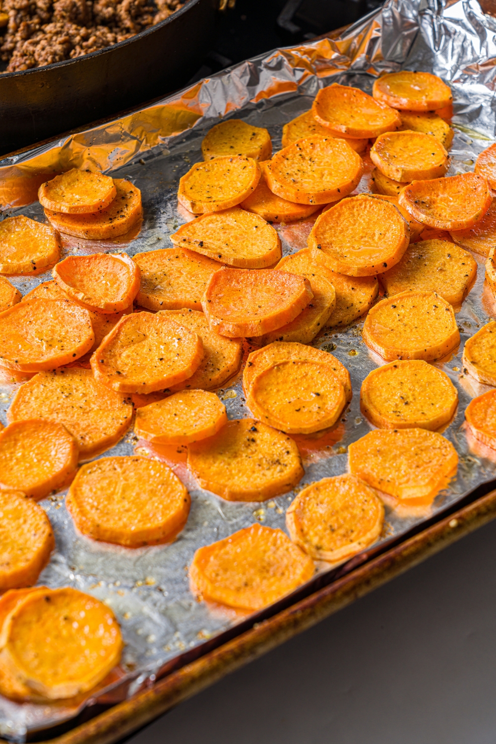 A baking sheet lined with foil with baked sweet potato medallions.