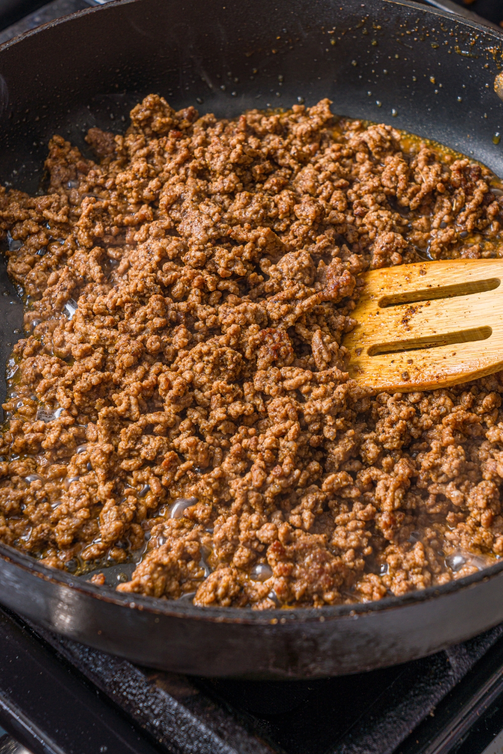 A skillet with a wooden spoon mixing a seasoned ground beef. The skillet is cooking on the stove.