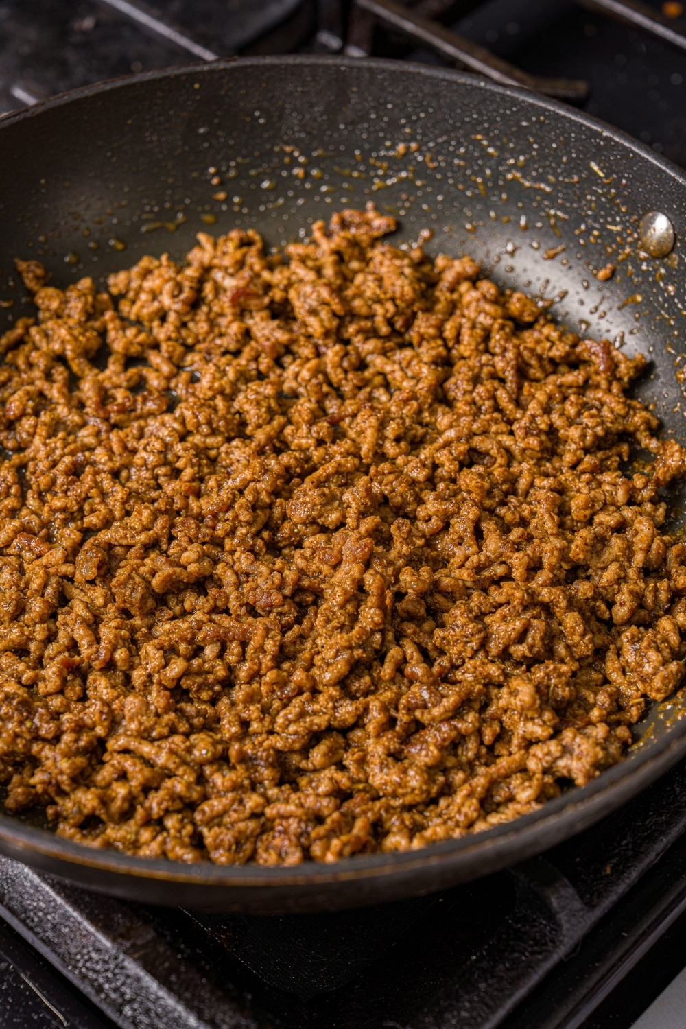 A skillet with seasoned ground beef. The skillet is cooking on the stove.