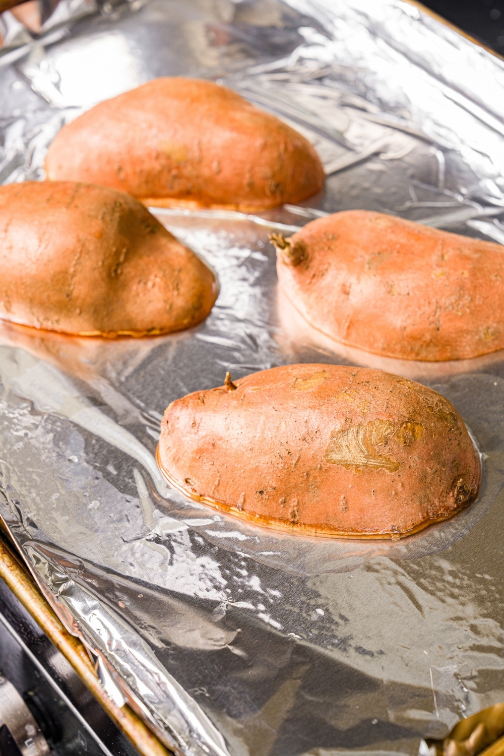 A baking sheet lined with foil with two sweet potatoes cut lengthwise facing down.