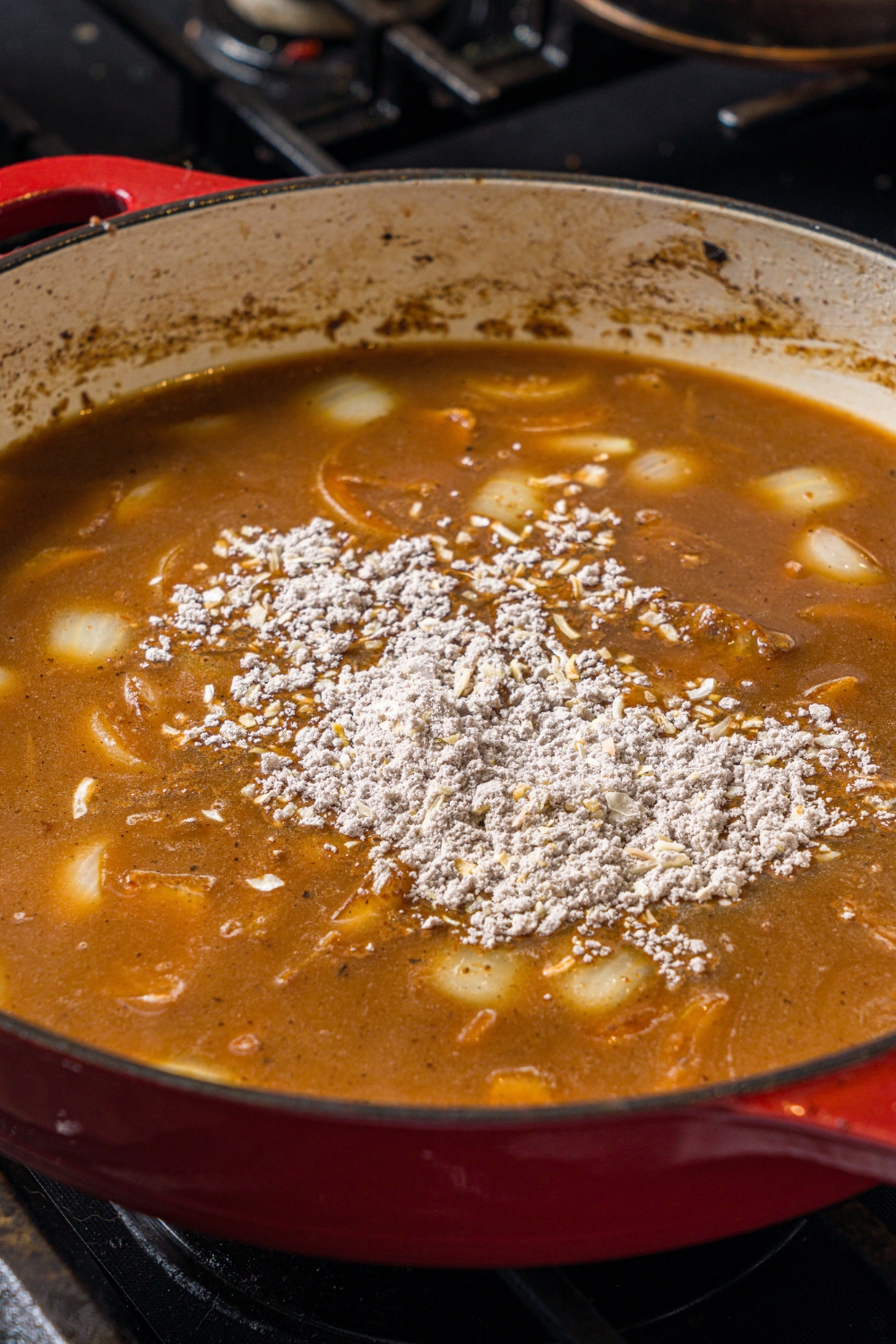 A cast iron skillet with an onion gravy base topped with soup mix. The skillet is cooking on a stove.