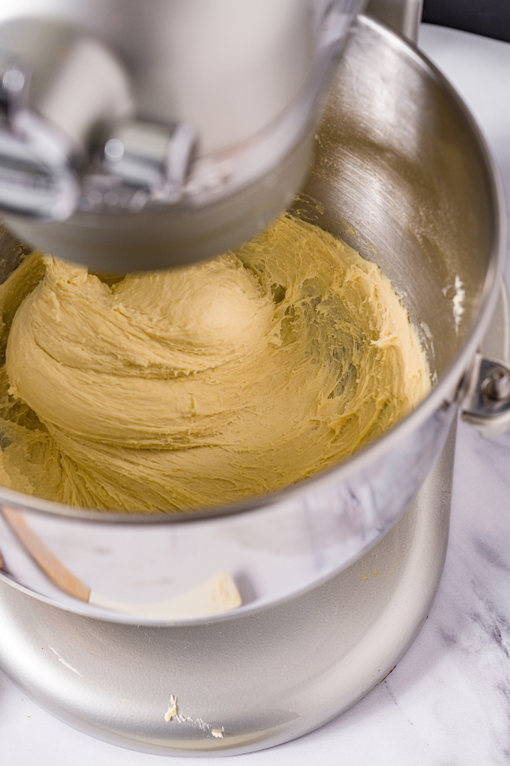 A stand mixer kneading beignet dough. The mixer is on a marble counter.