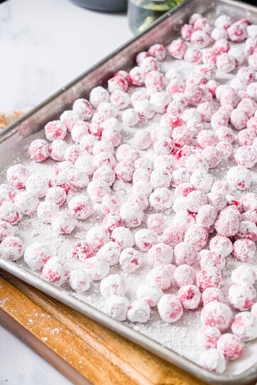 A baking sheet lined with parchment paper covered with sugar coated cranberries. The sheet is on a wooden board.