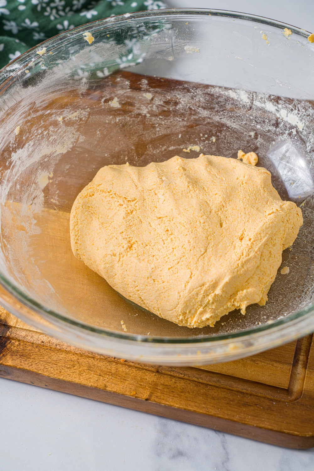 A glass bowl with a carrot noodle dough ball. The bowl is on a wooden board.