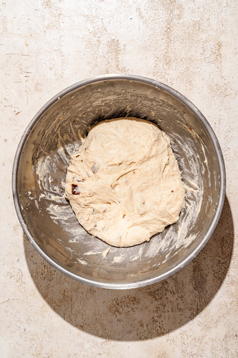 A large bowl with kneaded focaccia dough. The bowl is on a tan counter.