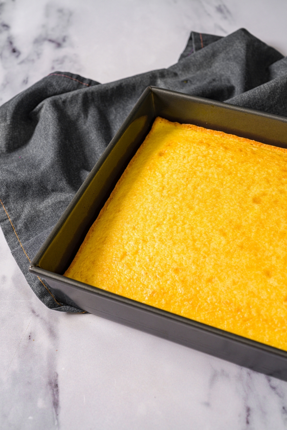 A baking pan with baked yellow cake. The pan is on a marble counter with a gray cloth napkin.