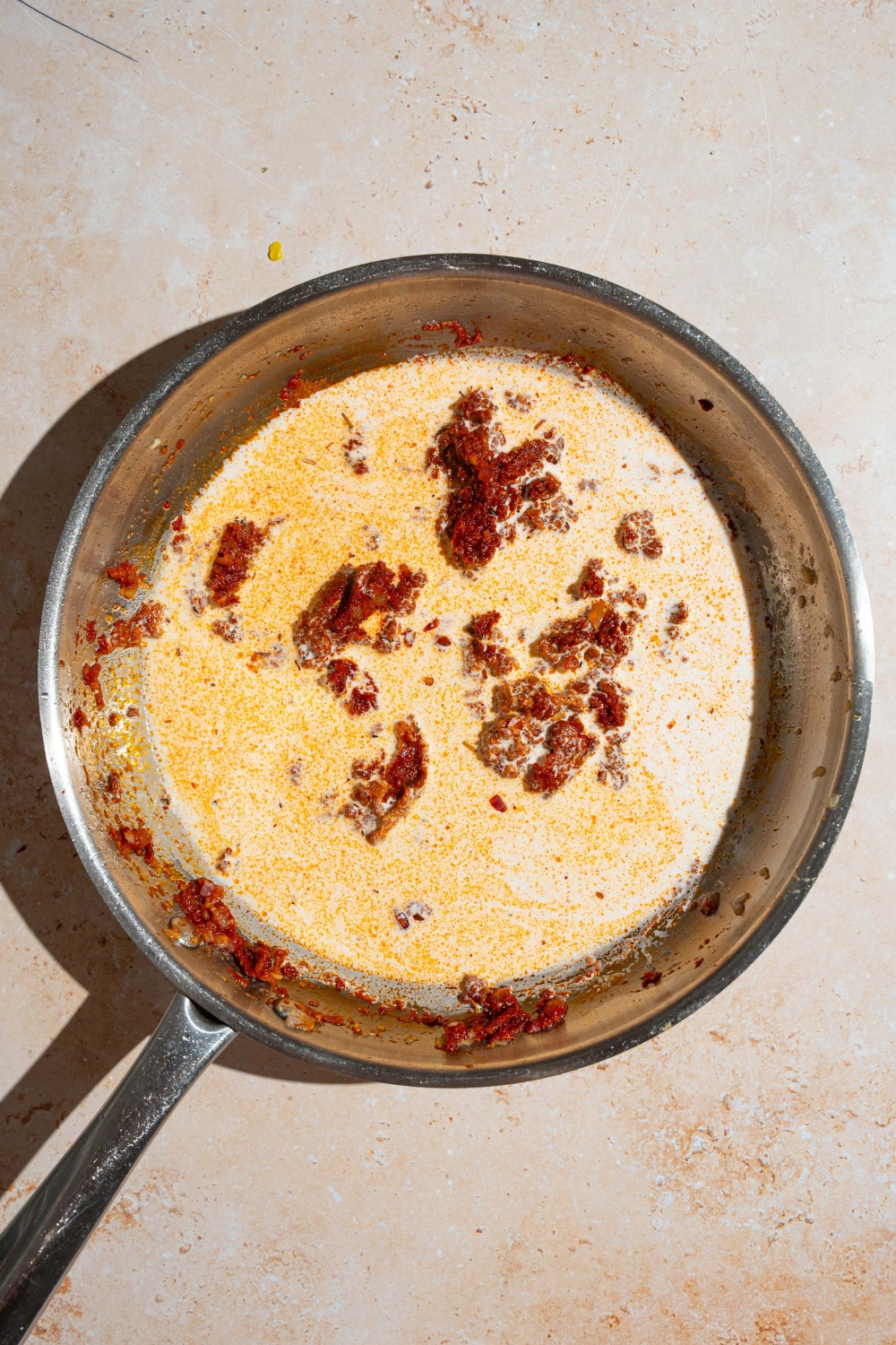 A skillet with sautéed garlic and onions with tomato paste and heavy cream. The skillet is on a tan counter.