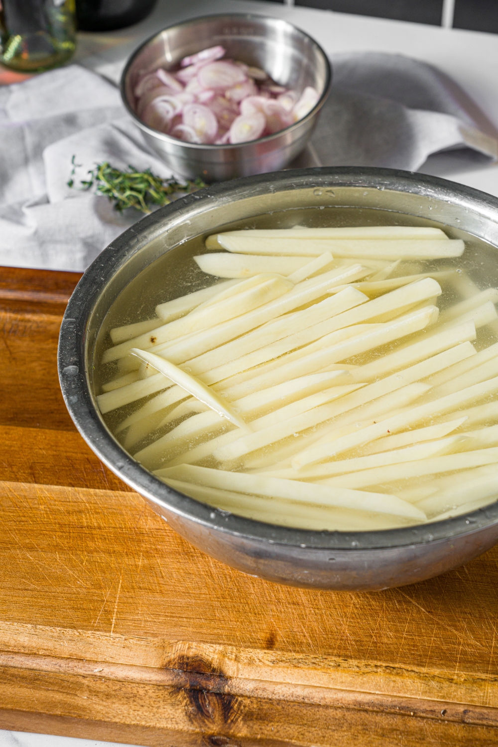 A large bowl of sliced potato fries submerged in vinegar. The bowl is on a wooden board.