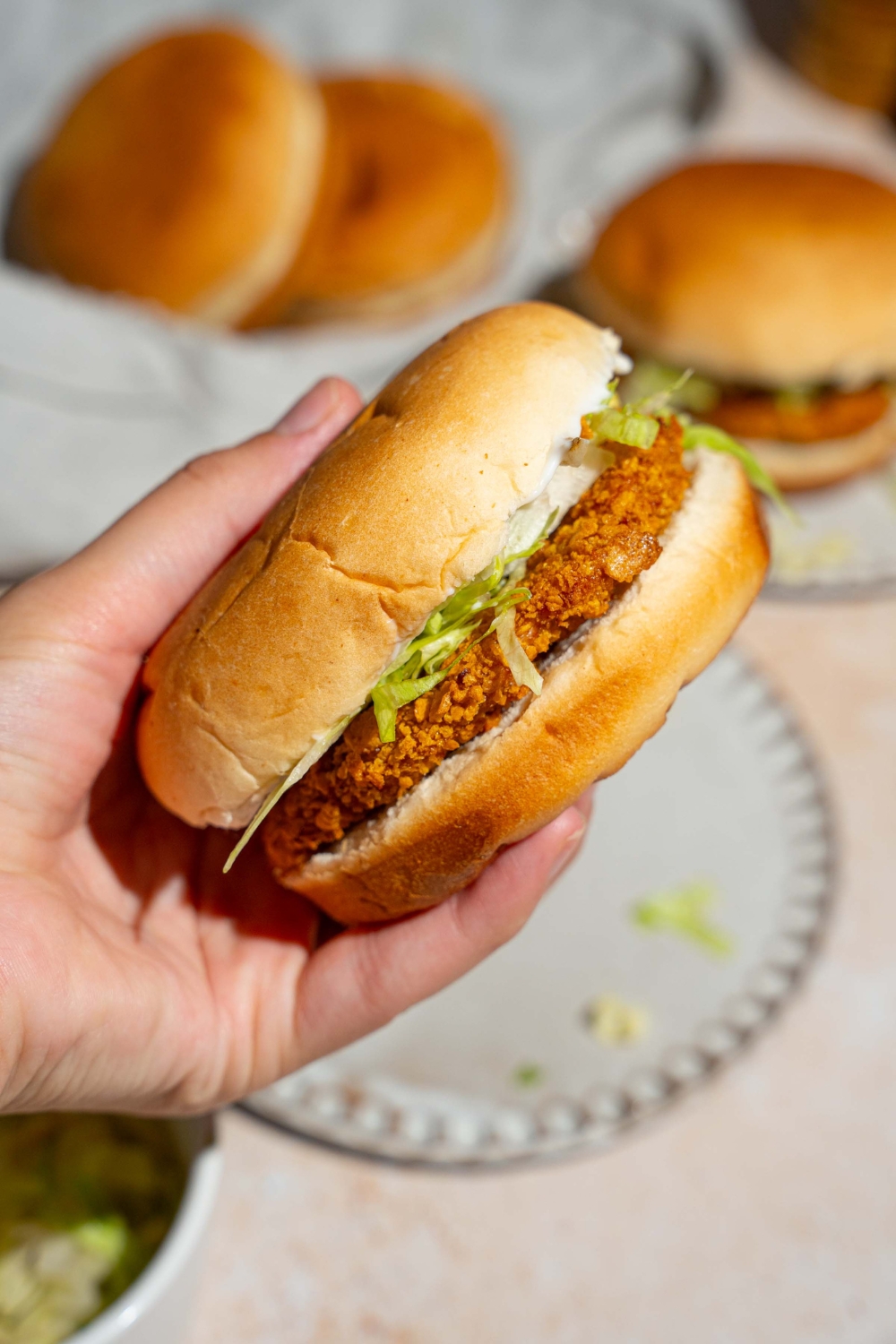 A close up of a hand holding a McChicken sandwich. There is a tan counter with an additional sandwich blurred in the background.