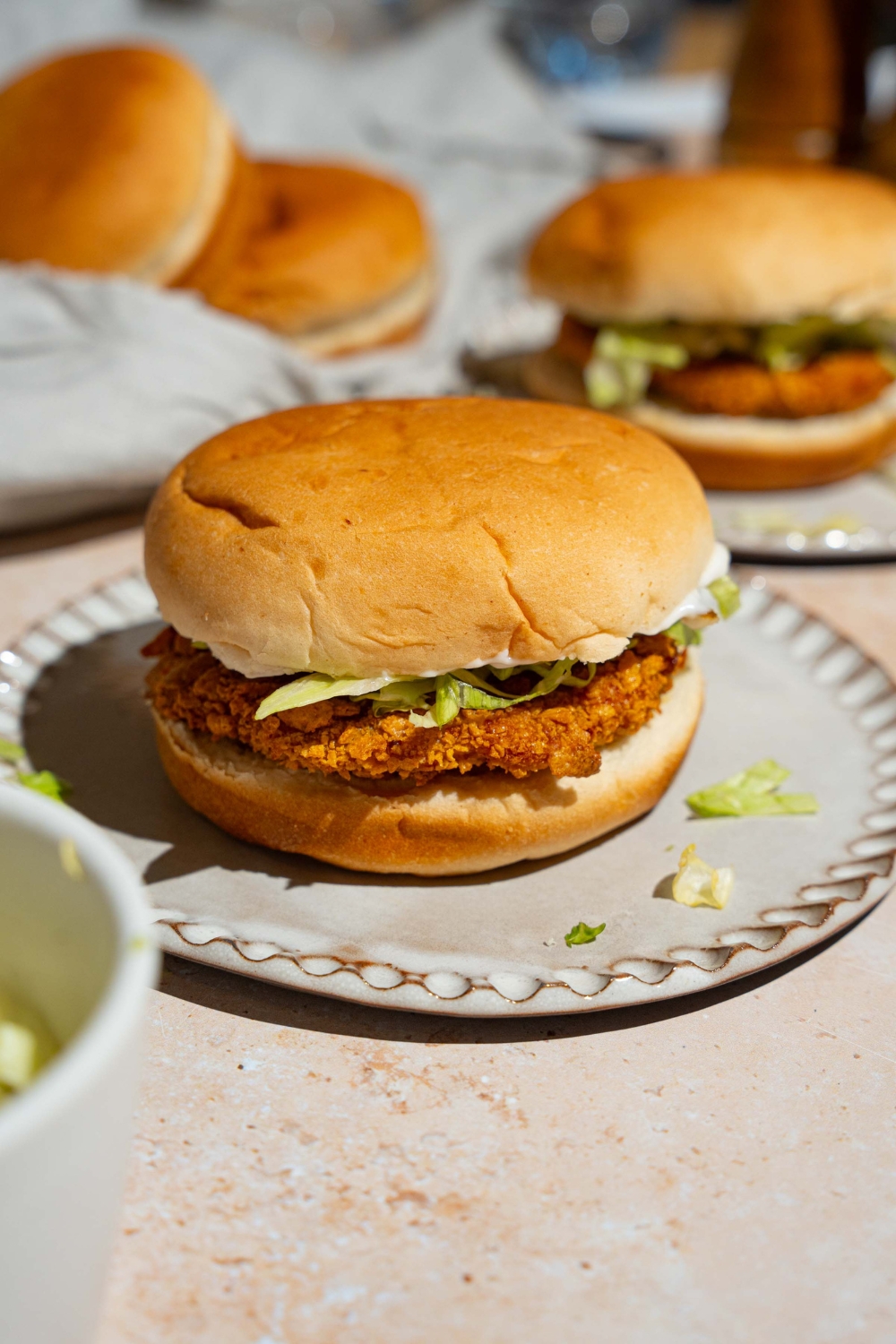 A plate with a McChicken sandwich. The plate is on a tan counter with an additional sandwich.