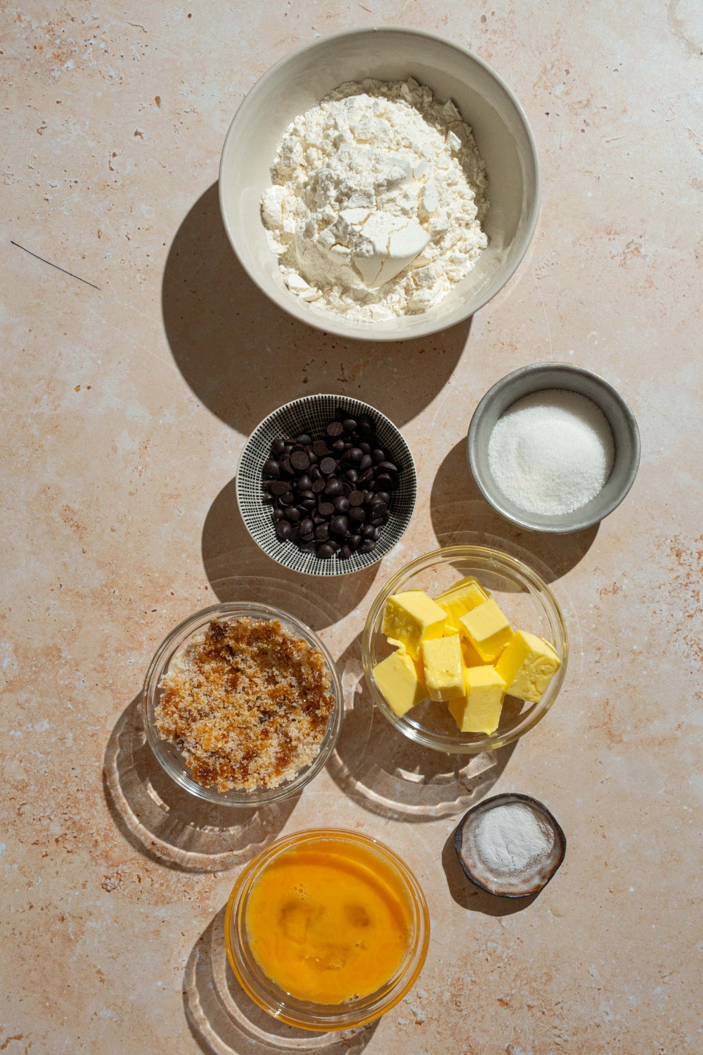 A tan counter with ingredients to make mini chocolate chip cookies including butter, brown sugar, sugar, flour, egg, vanilla, and chocolate chips.