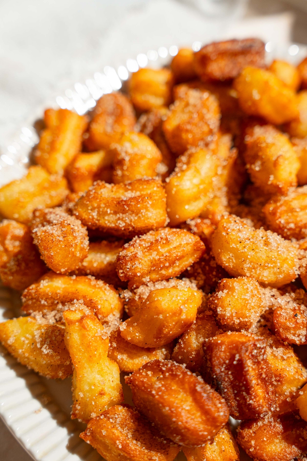A white plate with mini churros coated in cinnamon sugar. The plate is on a tan counter.