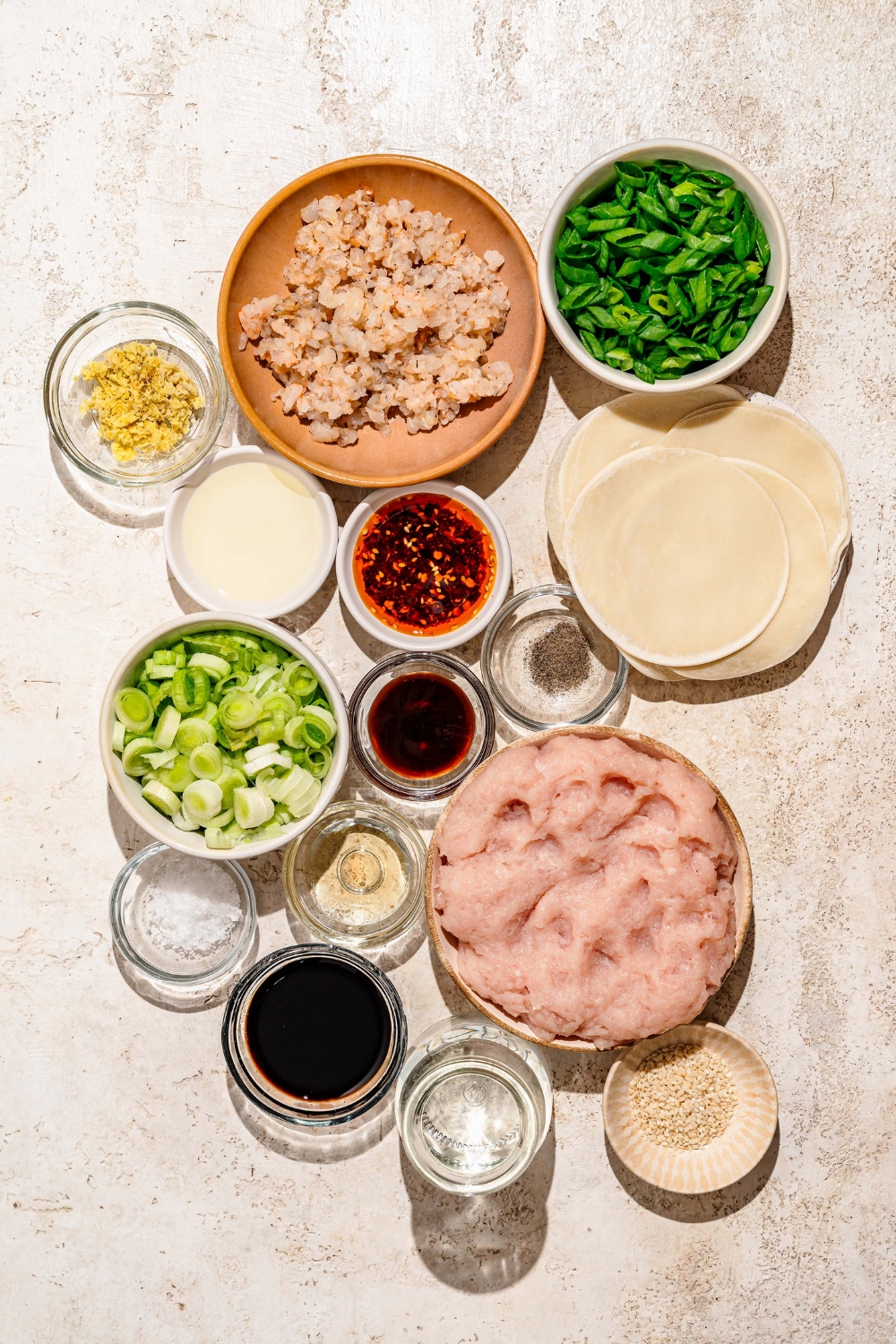 A tan counter with ingredients to make pan fried pork and shrimp dumplings including ground pork, chopped shrimp, green onion, leek, soy sauce, oyster sauce, sesame oil, ginger, dumpling wrappers, and more.