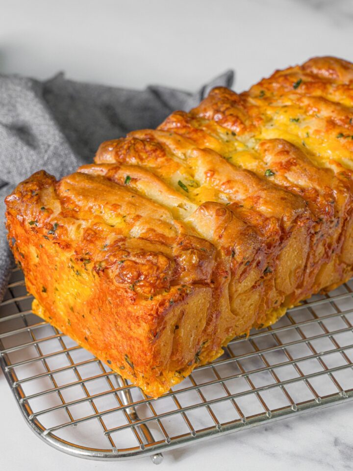 A loaf of pull apart, garlic bread on top of a wire rack that is on a white counter.
