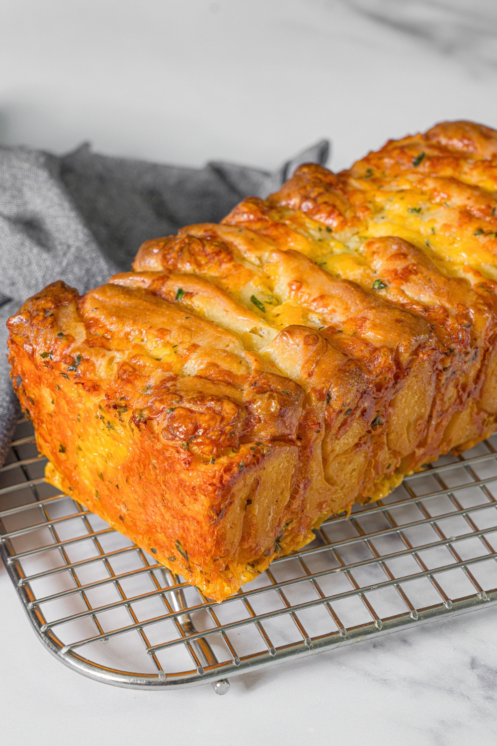 A loaf of pull apart, garlic bread on top of a wire rack that is on a white counter.
