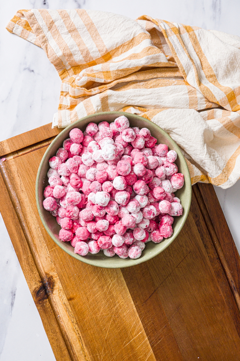 A green bowl with candied cranberries on a wooden board with a yellow striped napkin.