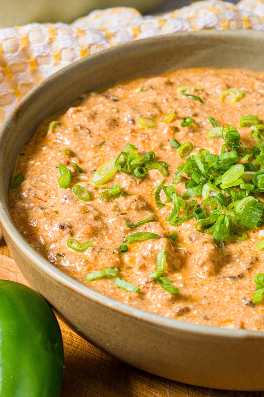 A bowl of divorced dad dip garnished with sliced green onion on a wooden board with a jalapeño.