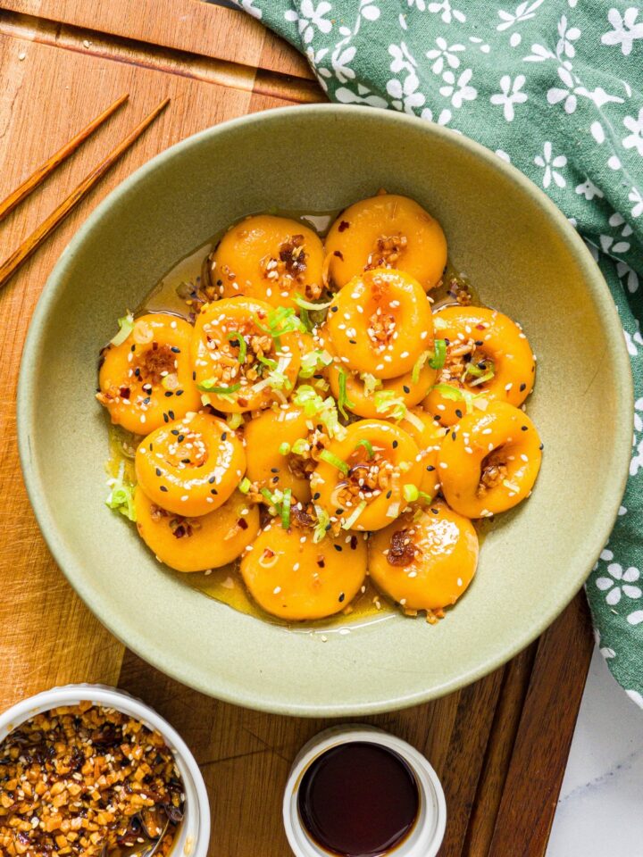 Carrot button noodles with chili crisp sauce on top in a green bowl.