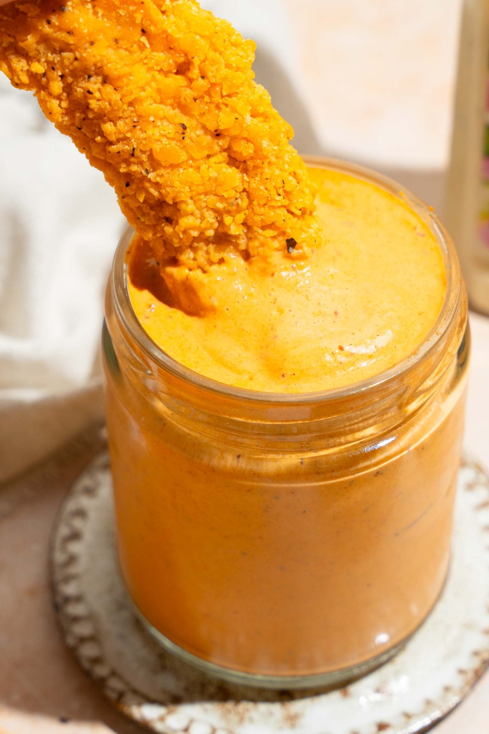 A chicken strip submerged in southwest chipotle ranch sauce in a glass jar.