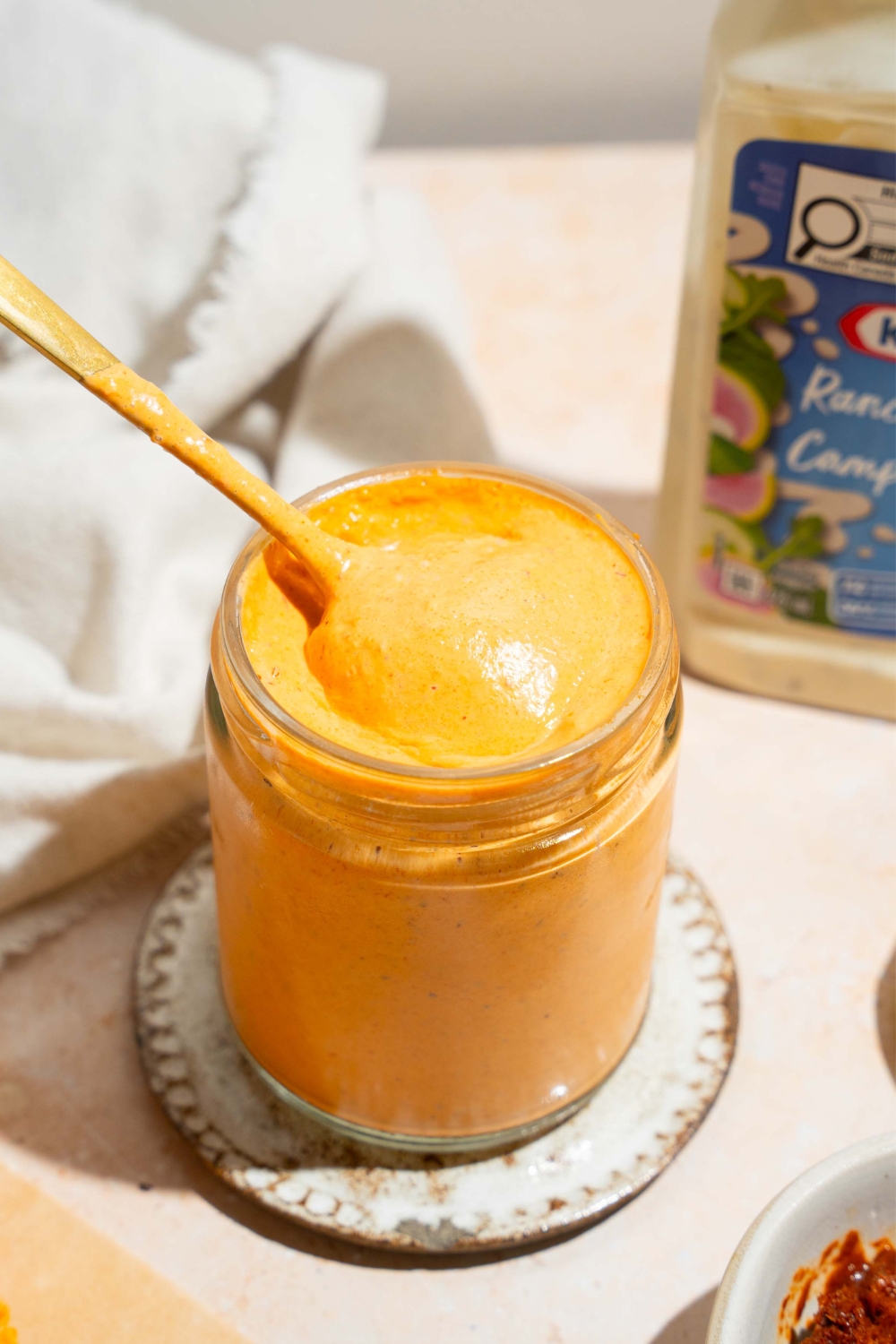 Spoon scooping southwest chipotle sauce out of a glass jar that is filled with the sauce.