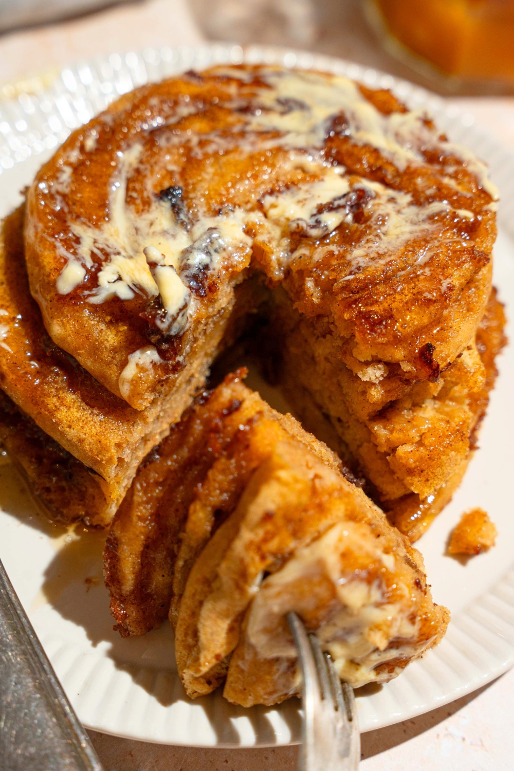 A stack of four cinnamon roll pumpkin pancakes with a portion cut out of the front. That portion is on a fork in front of the stack all on a white plate.