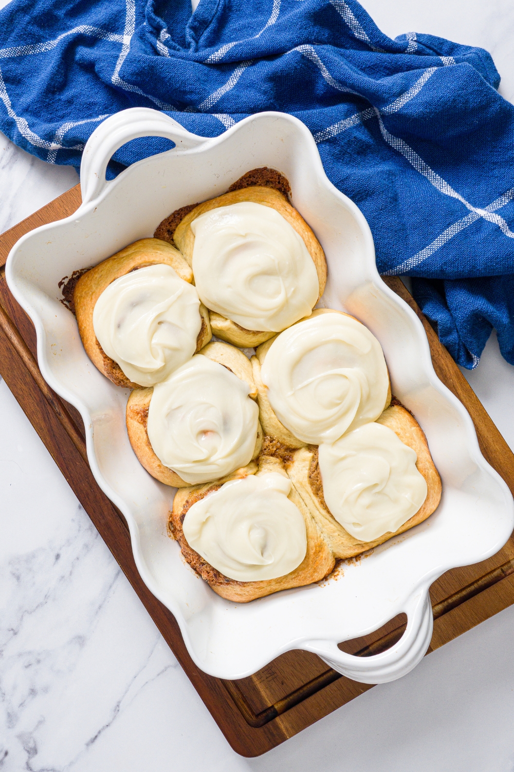 Six frosted cookie dough cinnamon rolls in a white baking dish.