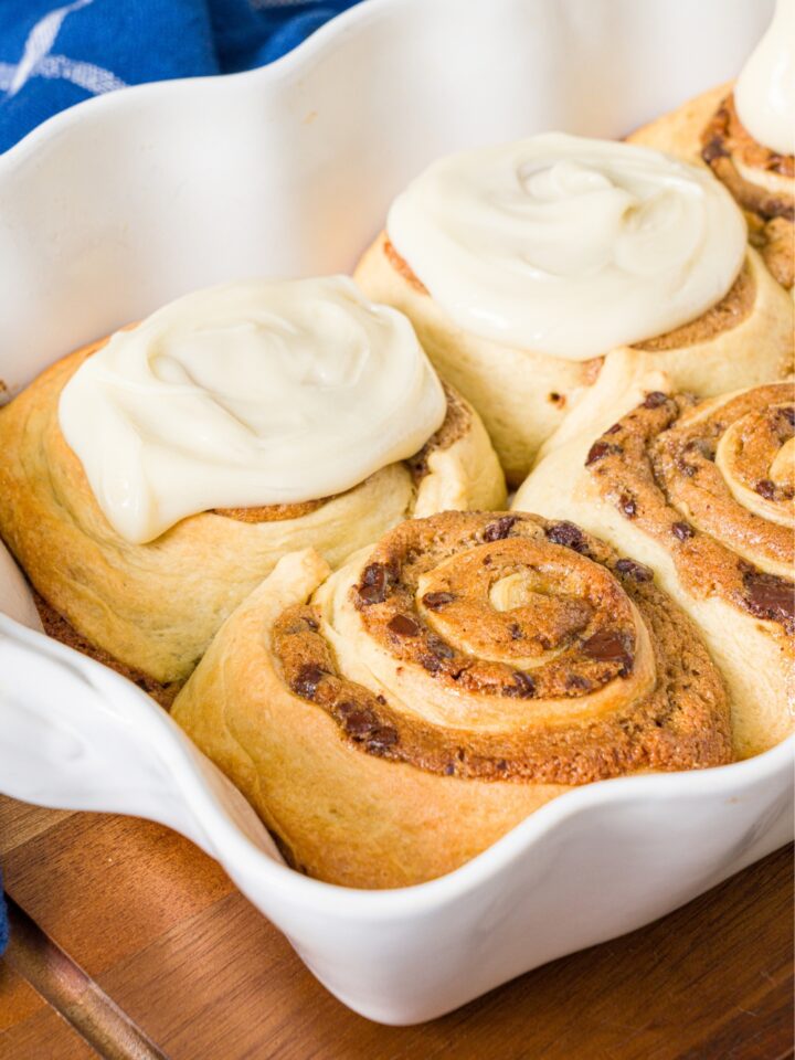 Two cookie dough, cinnamon rolls with two frosted cookie dough, cinnamon rolls behind it all in a white tray.