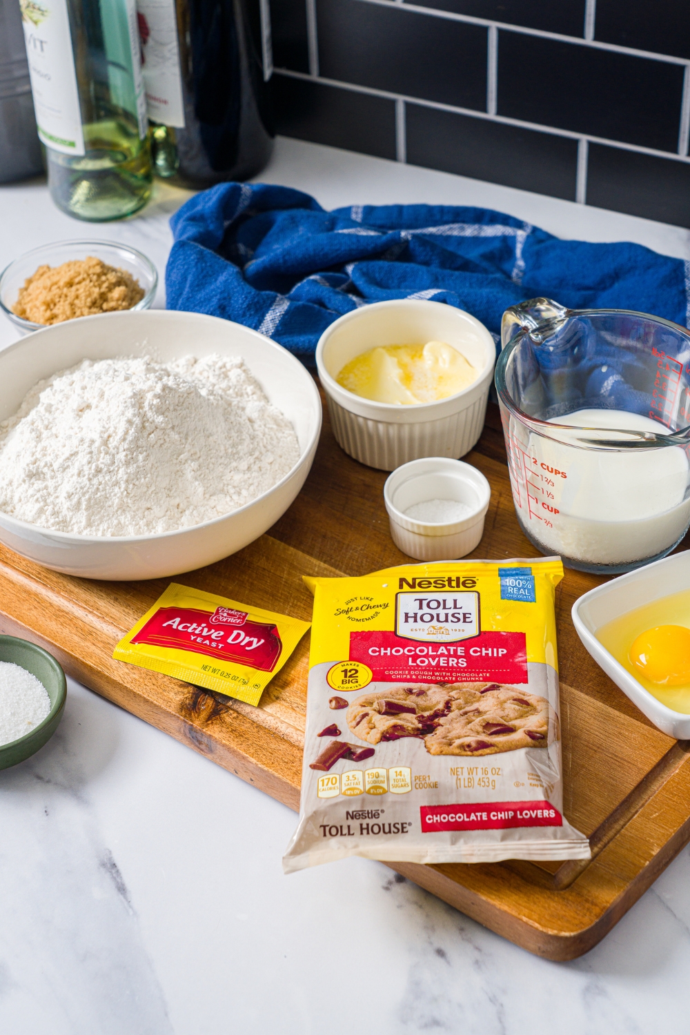 A package of Nestlé Tollhouse chocolate chip lovers cookie dough, a package of active yeast, a bowl of flour, a bowl of butter, a picture of milk, and a bowl with eggs in it.