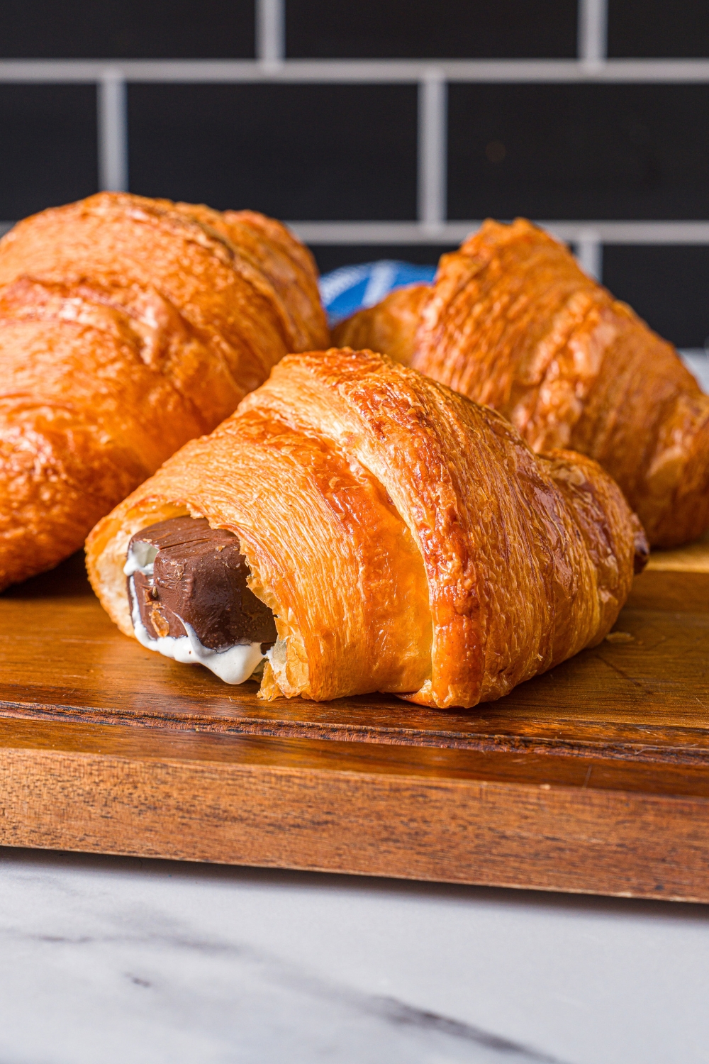 A croissant ice cream sandwich on a wood cutting board with two croissants behind it.