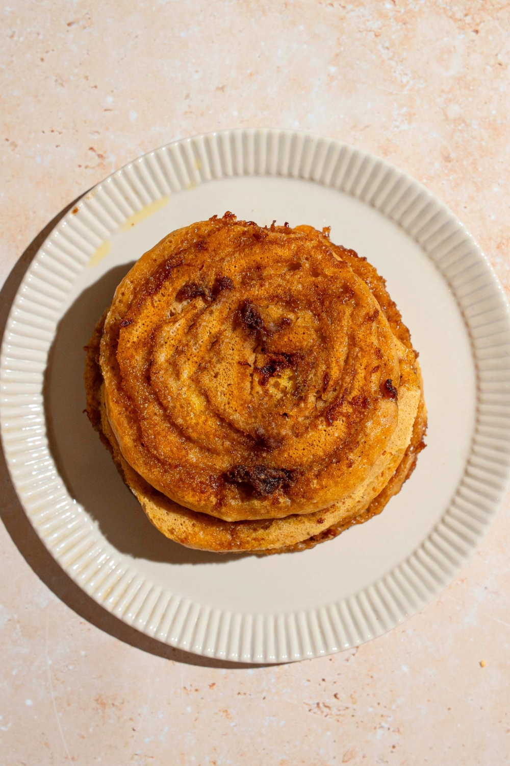 Cinnamon roll pumpkin pancakes stacked on a white plat.e