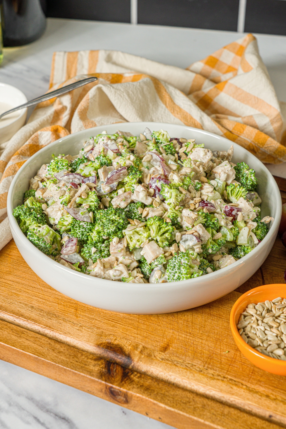 A healthy high protein broccoli chicken salad in a white bowl on top of a wooden cutting board.