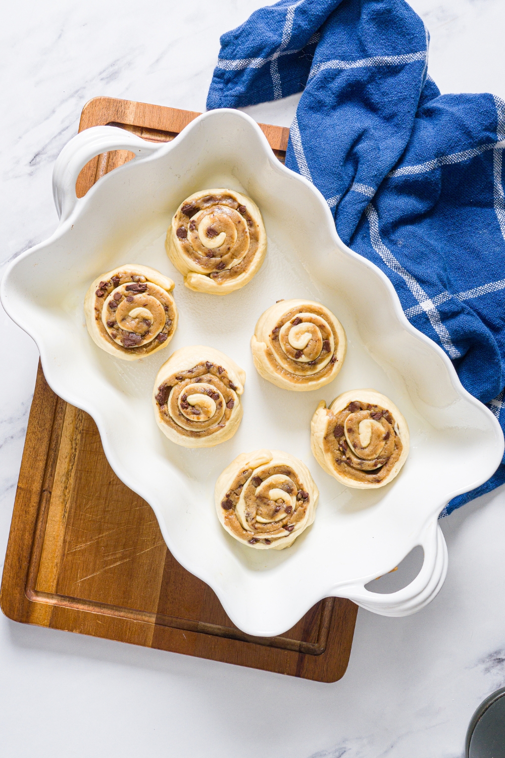 Six unbaked cookie dough, cinnamon rolls in a white baking dish.
