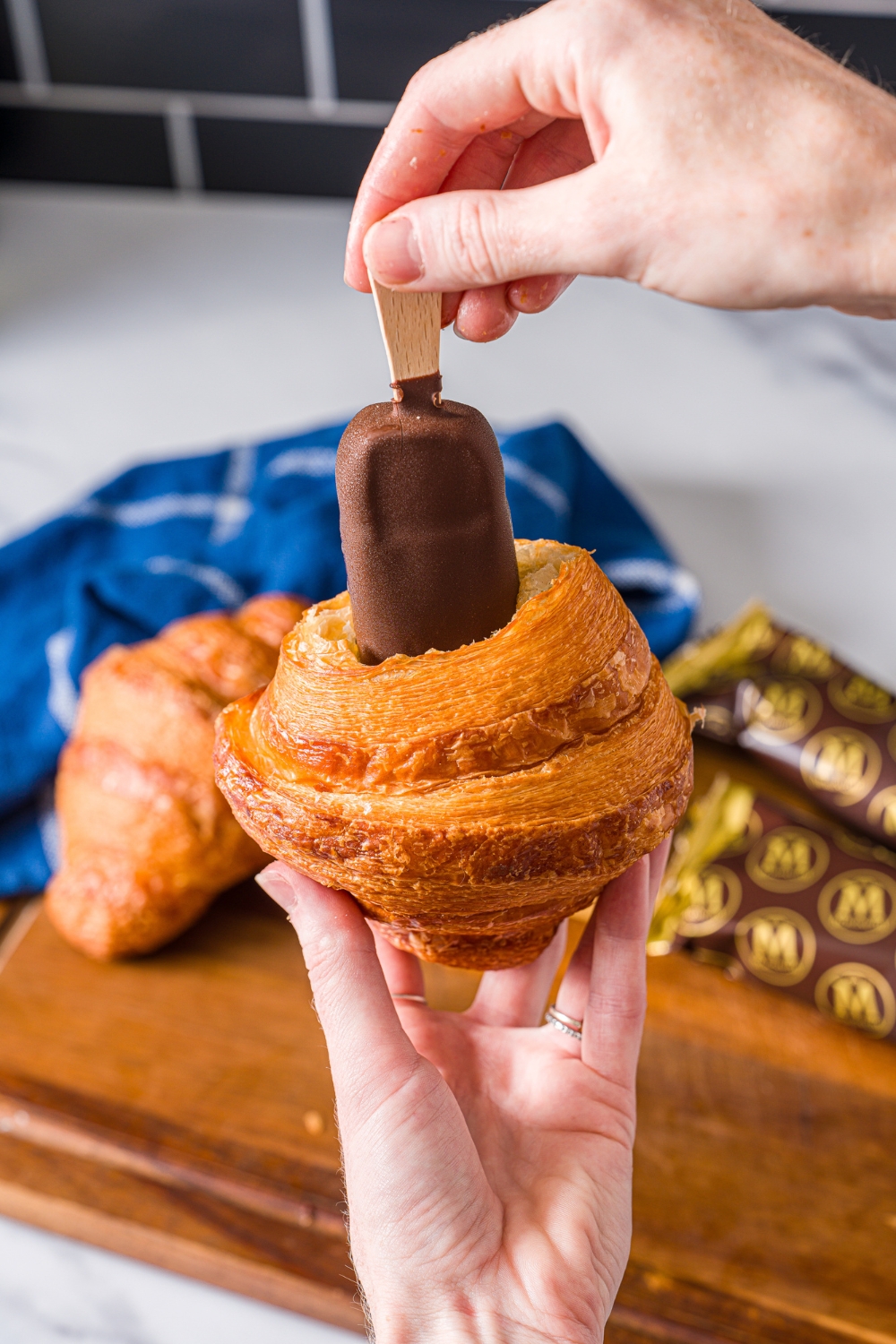 A hand holding a magnum ice cream bar upside down shoving it in a croissant.