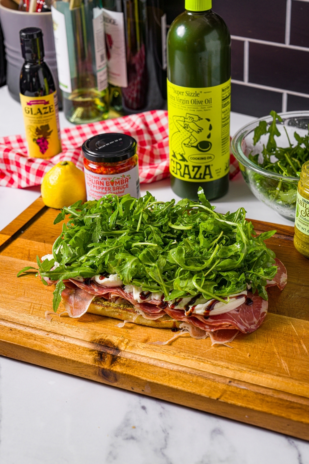 Arugula, layered on top of burrata and deli meat on a slice of focaccia bread on a wooden cutting board.
