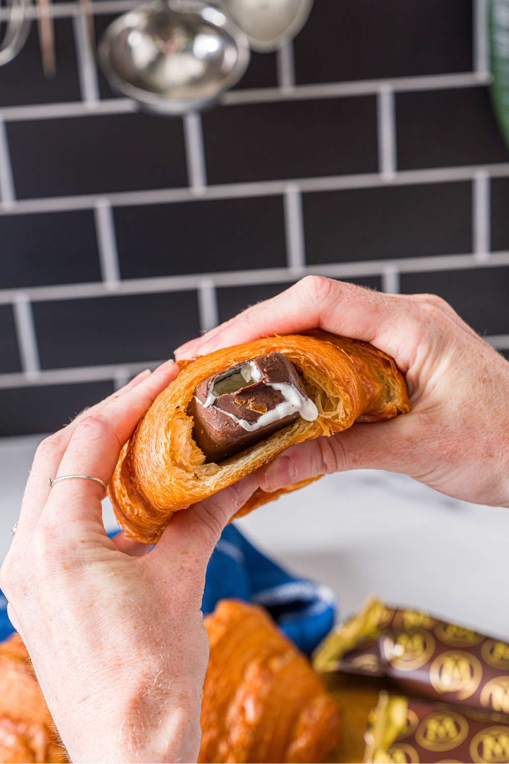 Two hands holding a croissant ice cream sandwich.