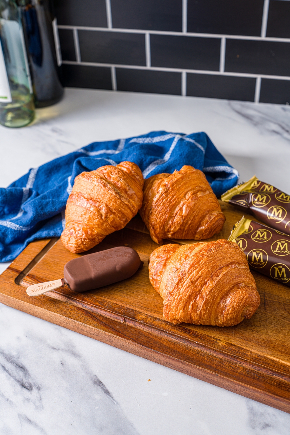 Three croissants and a magnum ice cream bar on a wood cutting board.