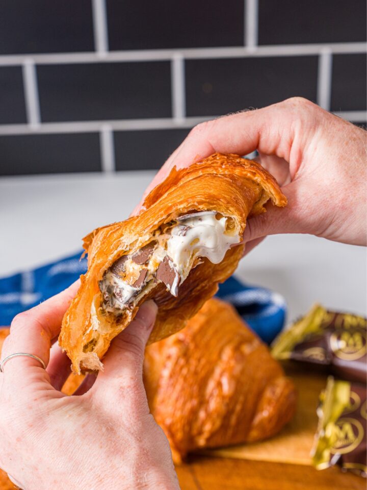 Two hands holding and smushing an ice cream bar in a croissant.