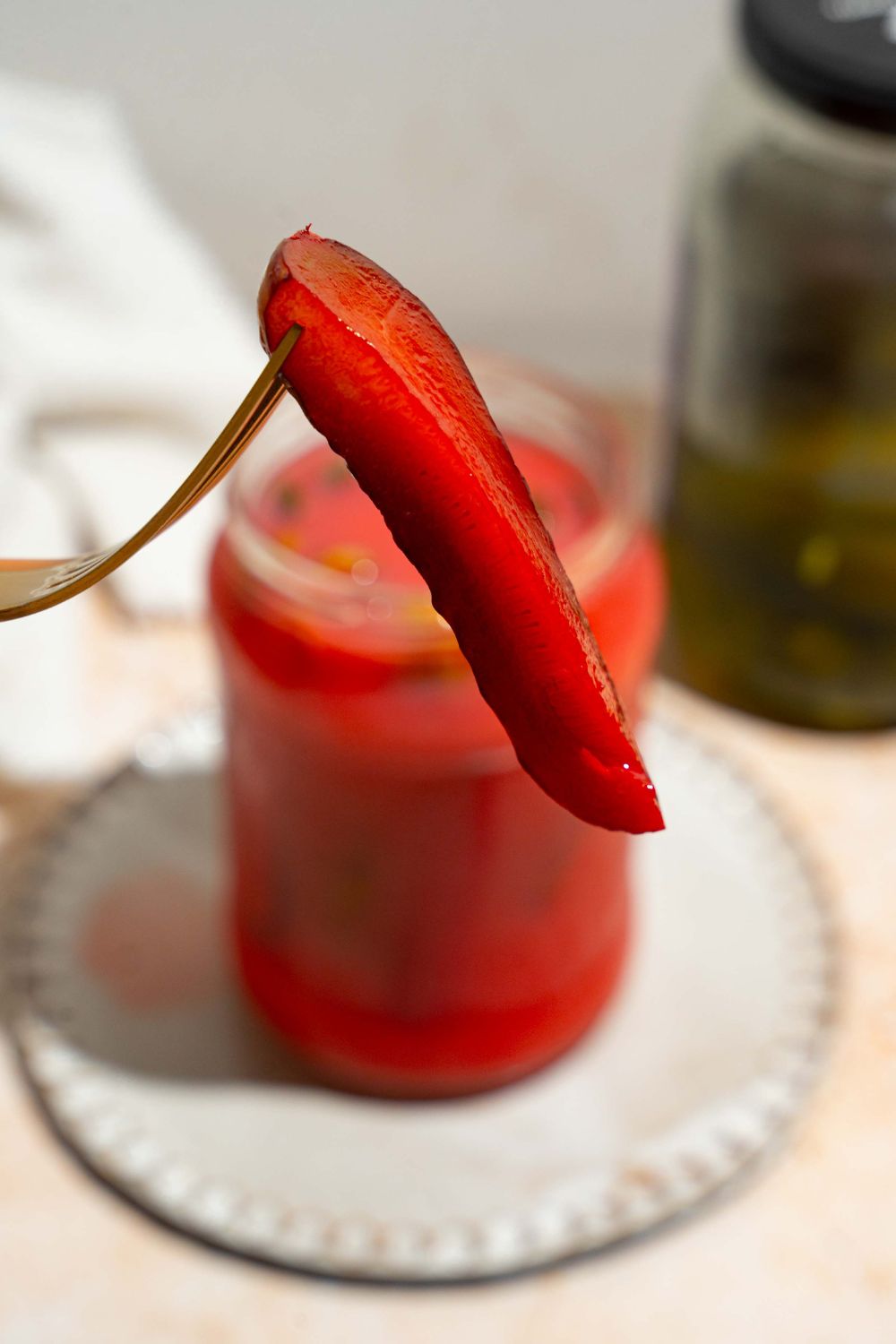 A close up of a fork holding a kool aid pickle with a jar of pickles on a tan counter blurred in the background.