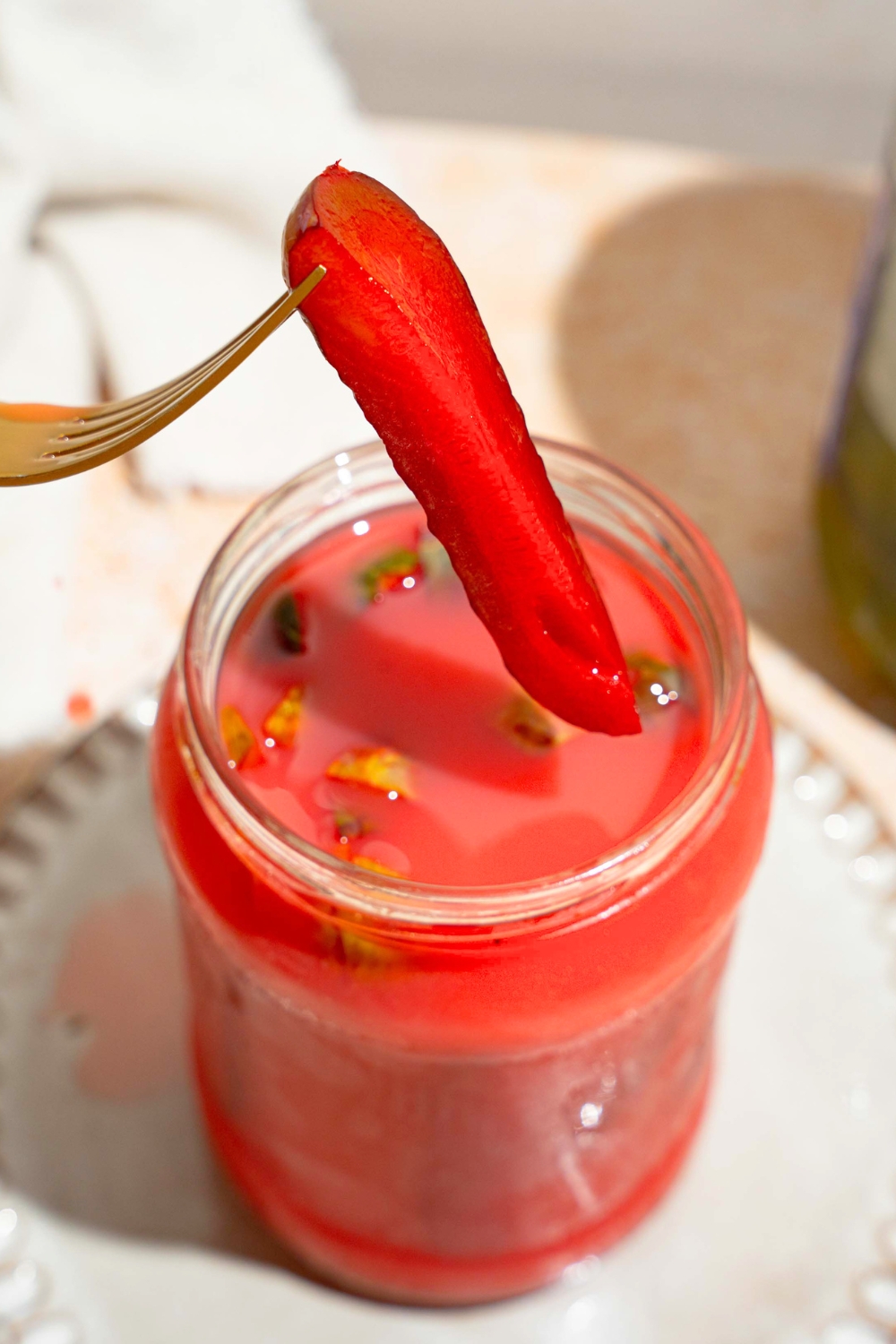 A kool aid pickle spear with a fork in it being held above a jar that is filled with the koolickles.