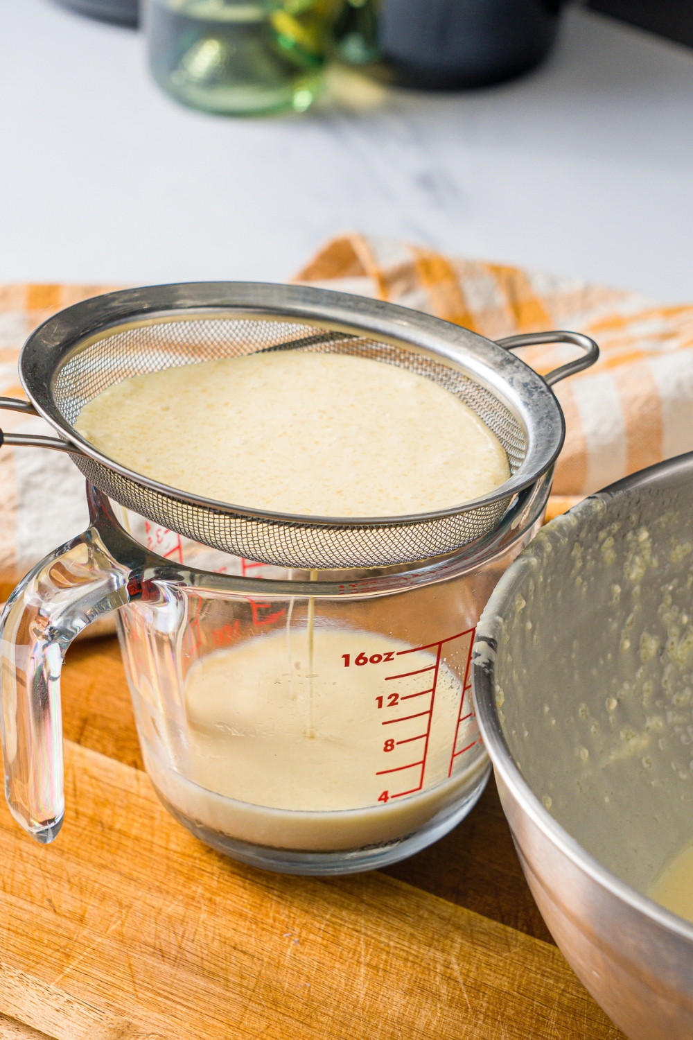 A mesh sieve with mango pancake batter in it draining into a glass measuring cup.