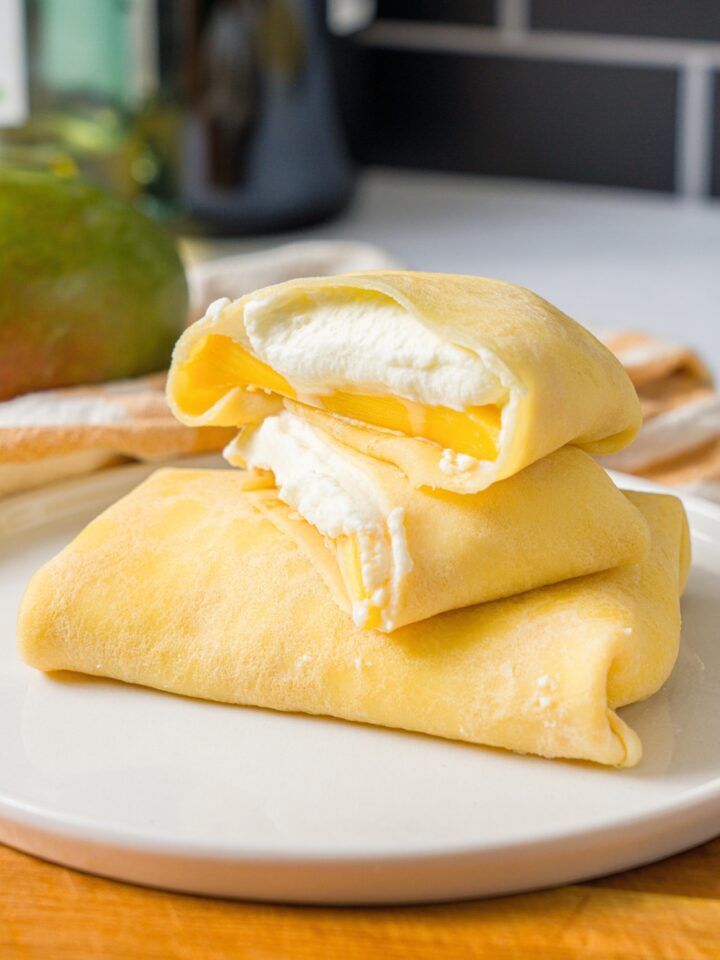 A mango pancake that is sliced in half with 2/2 on top of one another on a whole mango pancake that is on a white plate.