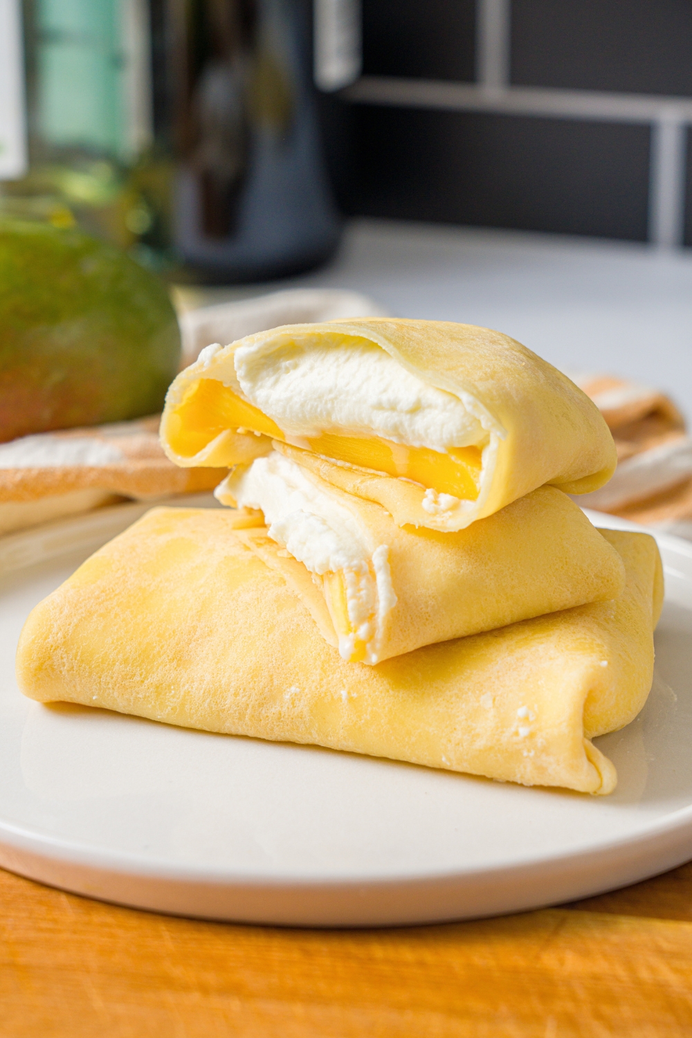 A mango pancake that is sliced in half with 2/2 on top of one another on a whole mango pancake that is on a white plate.