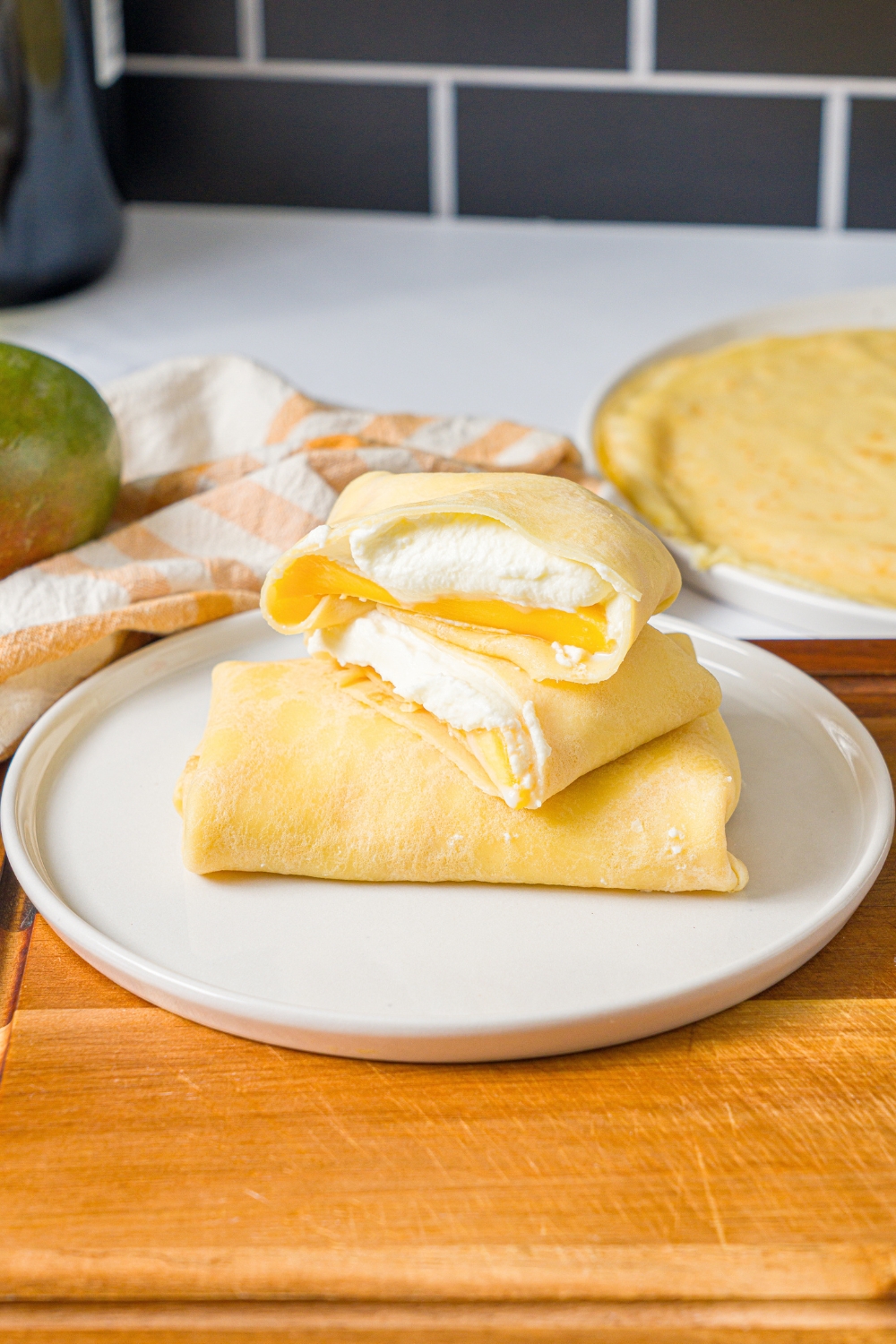 A cut mango pancake with 2/2 stacked on top of one another on a whole mango pancake on a white plate on a wooden board.
